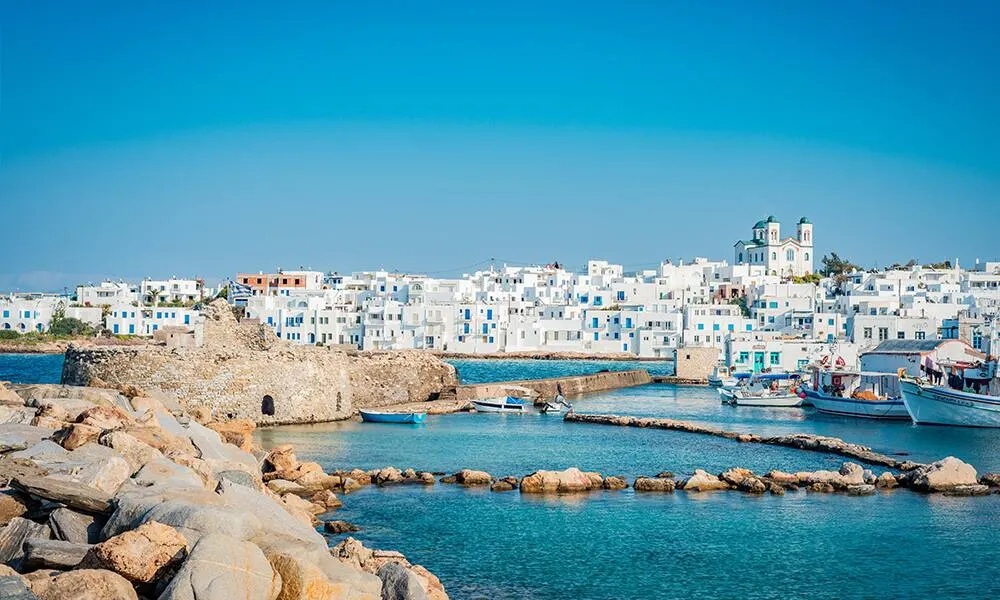 A whitewashed harbour town on a Greek island, with boats moored along a stone breakwater.