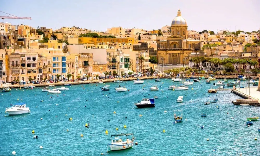 A harbour town in Malta, with waterfront buildings, a domed church and moored boats.
