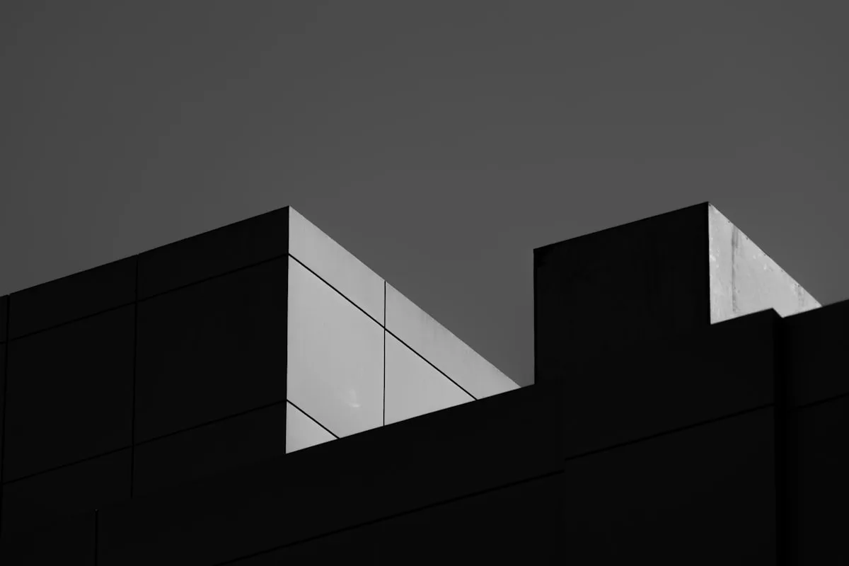 Sunlit and shadowed planes of a concrete building against a grey sky.