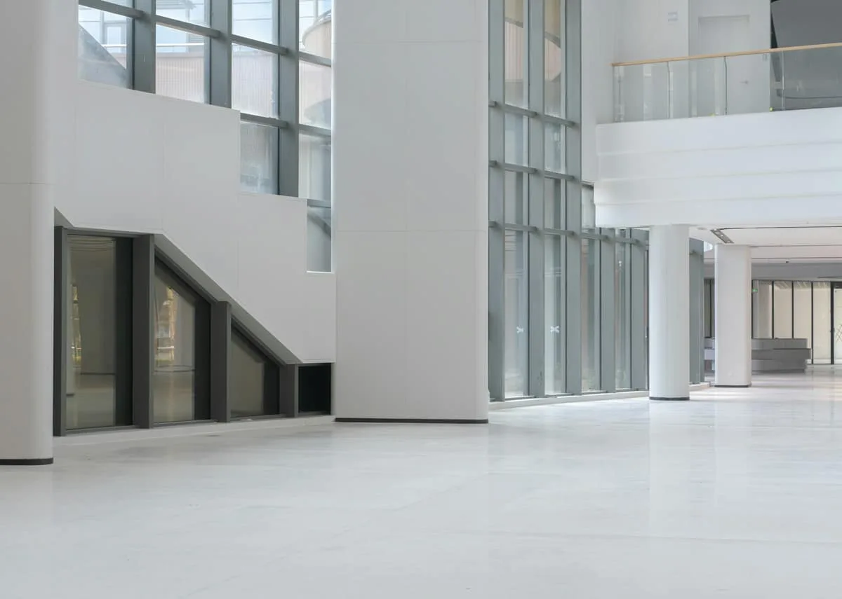 A bright, empty white atrium with columns and a full-height glass wall.