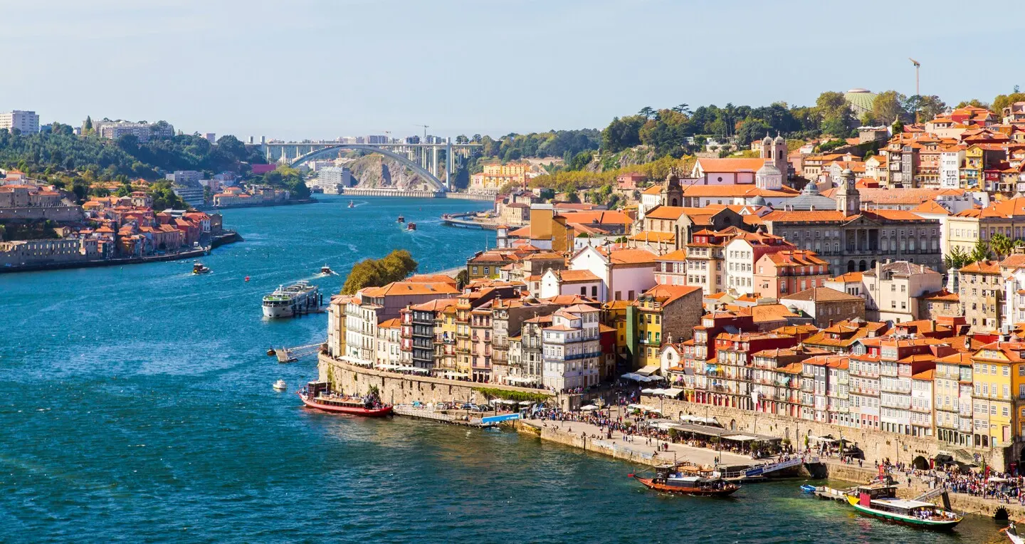 An aerial view of Porto, Portugal, with the Douro river, a bridge and the city's terracotta rooftops.