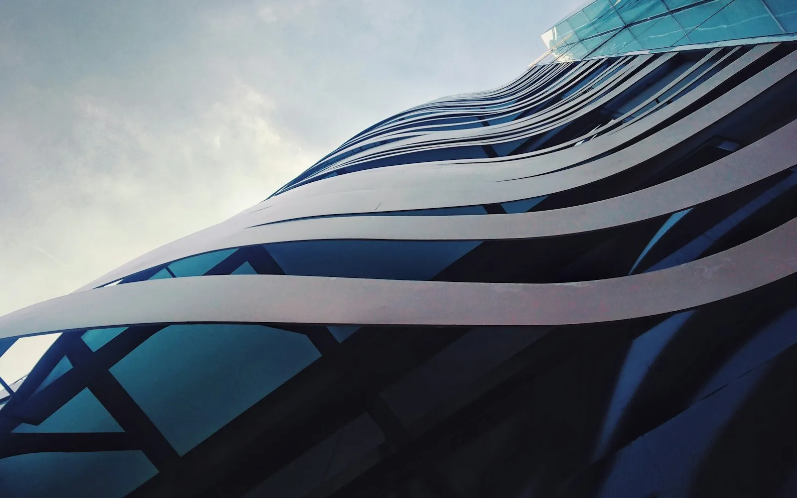 The curved glass facade of a high-rise seen from below.