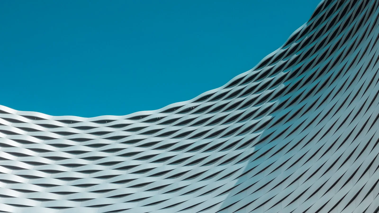 The woven metal facade of a building curving against a clear sky.