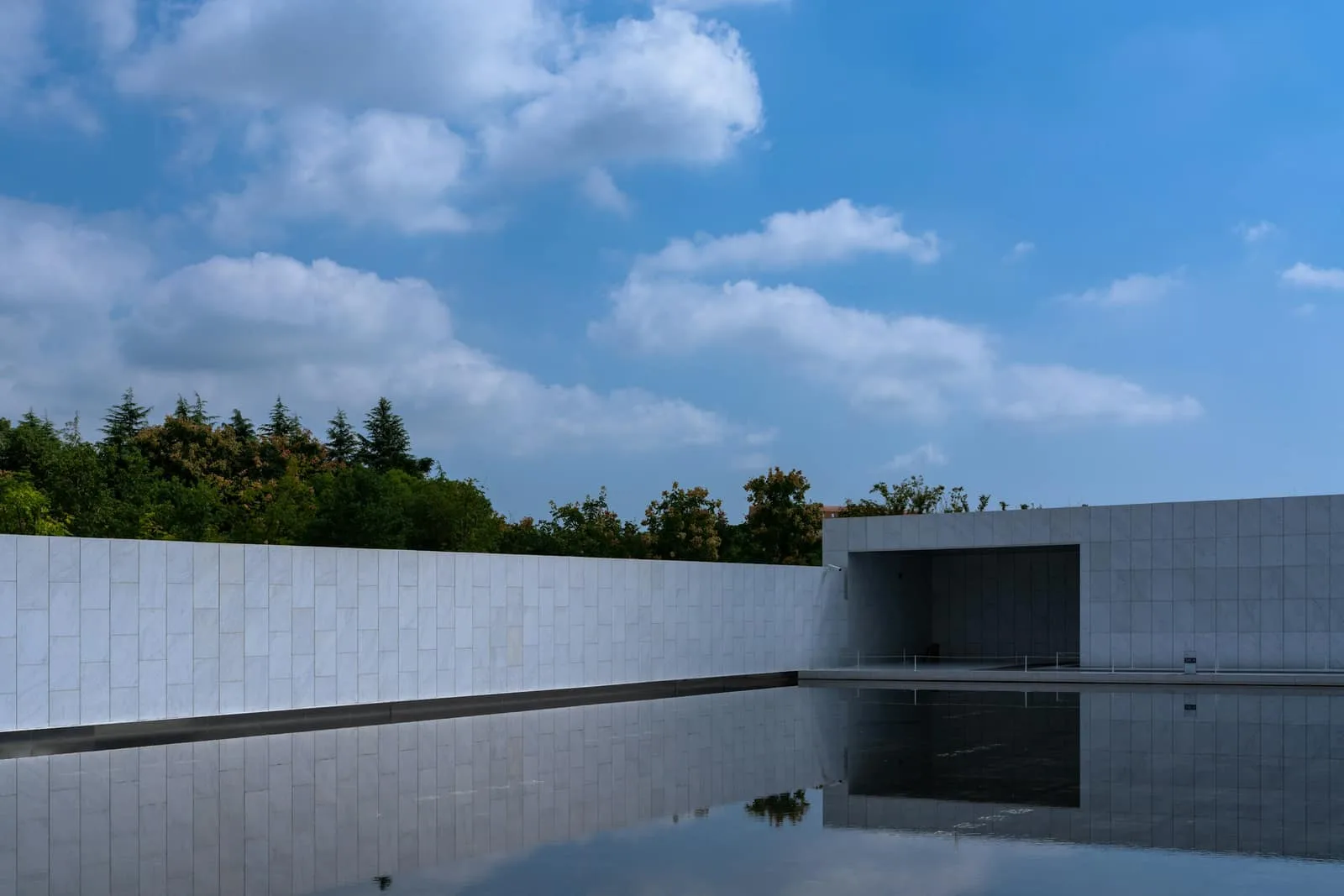 A low white stone building beside a still reflecting pool.