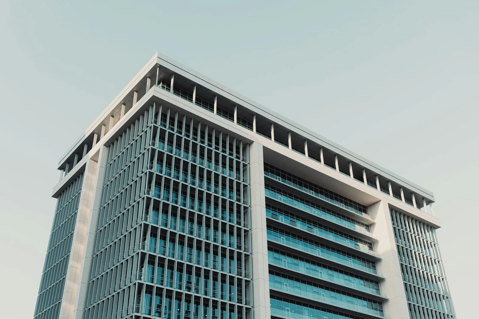 The upper floors of a finned high-rise seen from below against a pale sky.